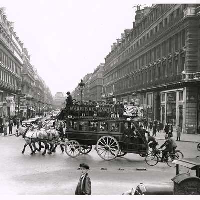 A horse-drawn omnibus carries passengers through a busy Paris boulevard in this early 19th-century photograph.