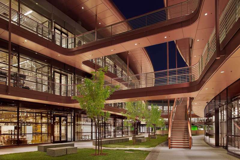 A modern, open-air courtyard features multiple levels, glass walls, and trees, illuminated at night.