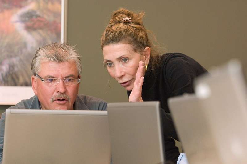 Christine Gabali helps Refugio Flores while looking at and pointing at laptop.