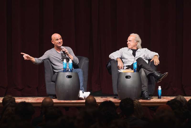 Andre Agassi gestures with a microphone during an onstage conversation with a seated interviewer.
