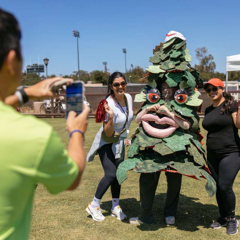 A person in the foreground takes a photo of two women standing with the Stanford Tree mascot