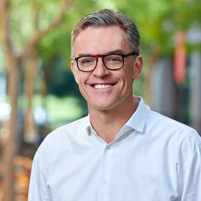 Hanno Lustig smiles for a professional headshot outdoors, wearing glasses and a button-down shirt.