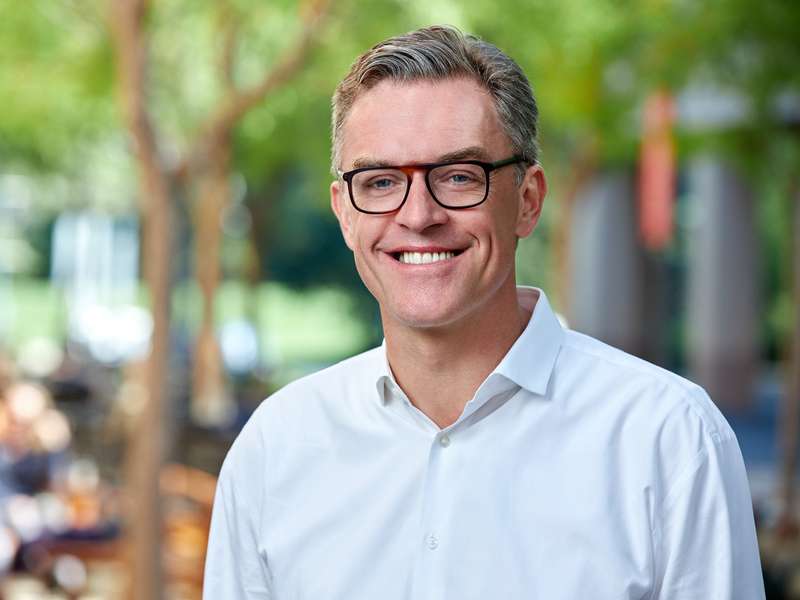 Hanno Lustig smiles for a professional headshot outdoors, wearing glasses and a button-down shirt.
