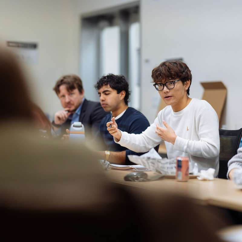 A group discusses ideas around a table, with one person animatedly speaking while others listen attentively during a meeting.