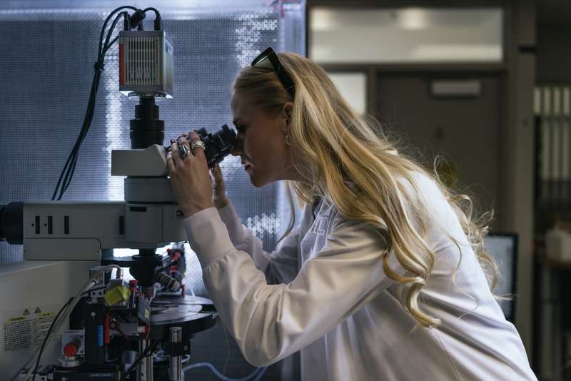 Annie Goettemoeller peers through a microscope in a darkened lab, laser safety glasses pushed up on her head.