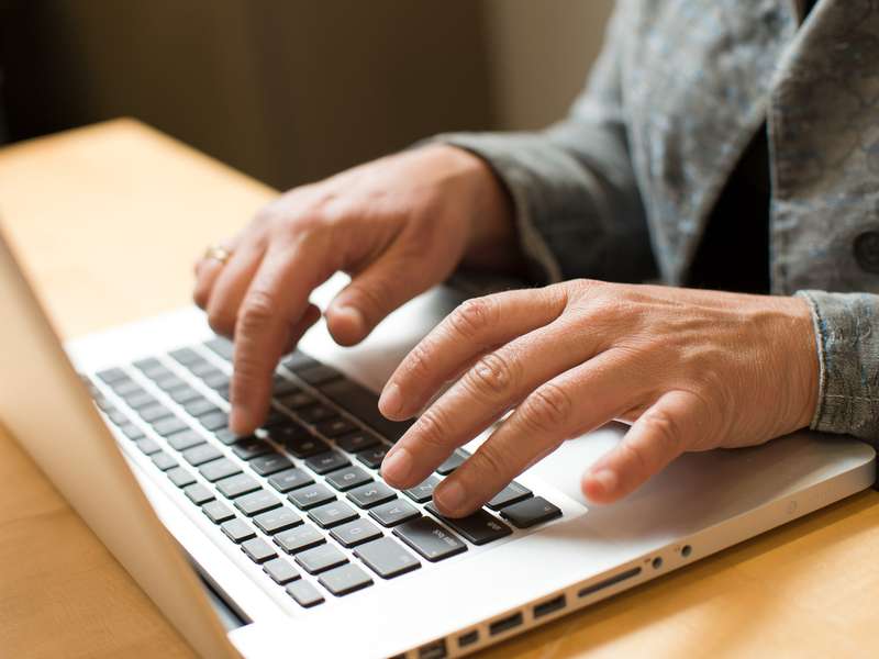 Two hands are shown typing on a laptop computer