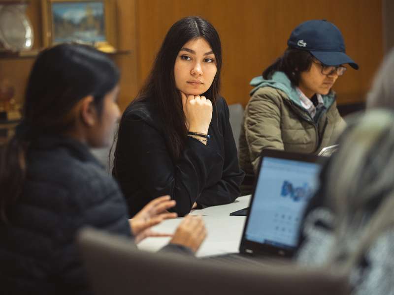 Students seated around a table listen attentively to one another during a discussion period in class.