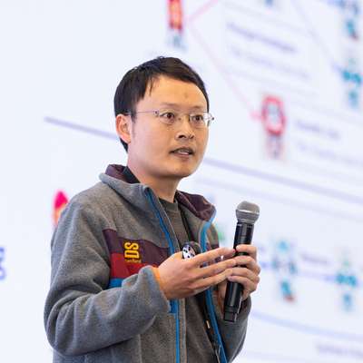 James Zou holding a microphone and gesturing while speaking at an event.