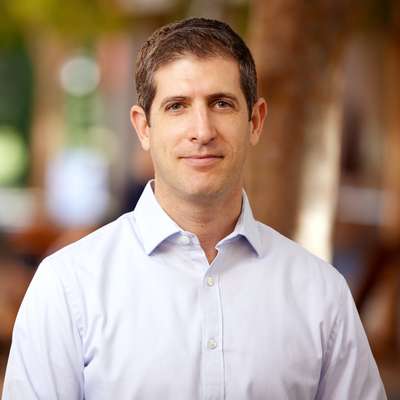 Nir Halevy poses for a portrait outdoors with a blurred courtyard behind him.