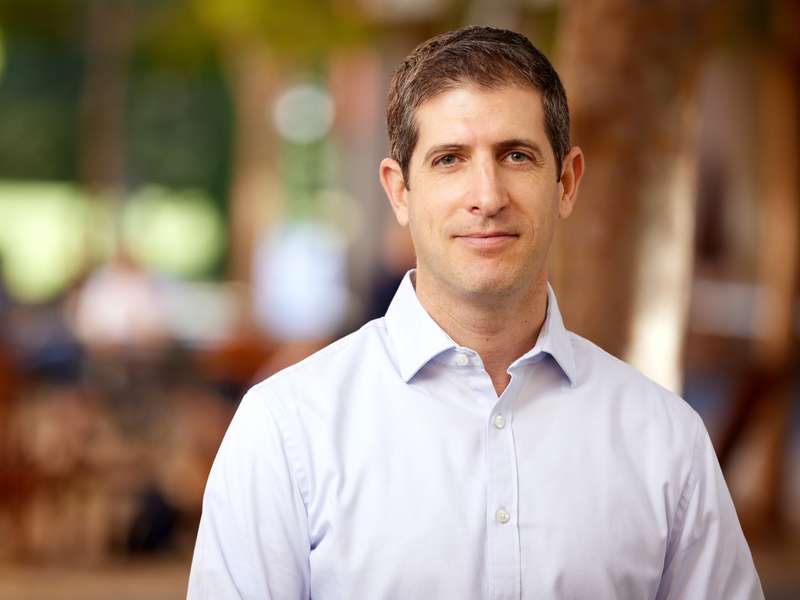 Nir Halevy poses for a portrait outdoors with a blurred courtyard behind him.