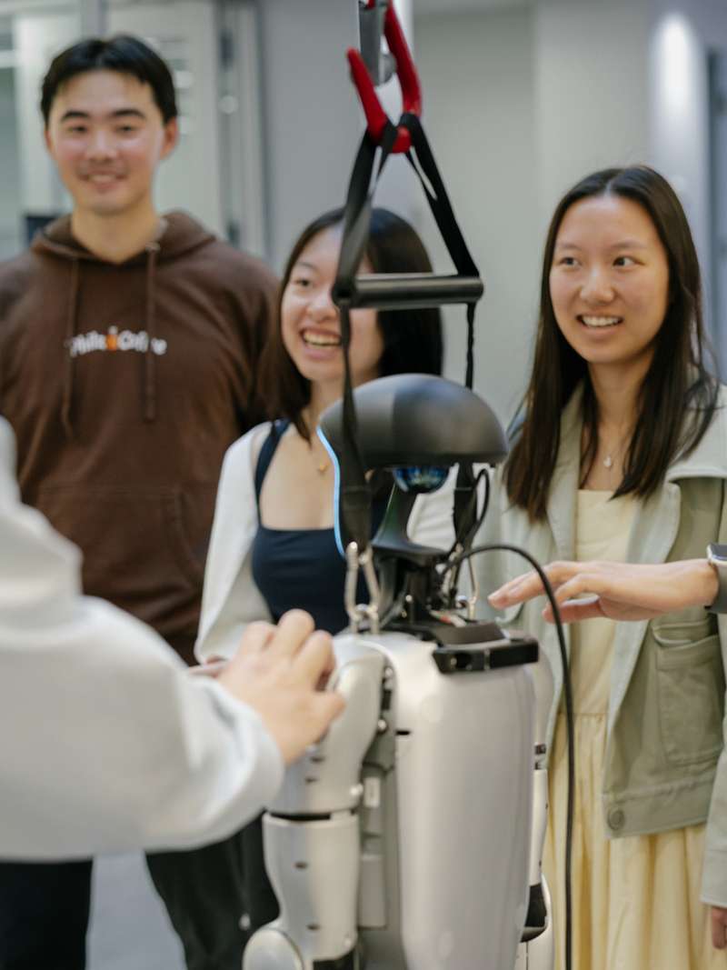 A group interacts with a humanoid robot in a lab setting, while one person explains its features to the others.