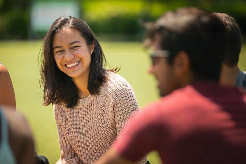 Jasmin Dalsgaard laughs during an outdoor conversation with peers on a sunny campus lawn.