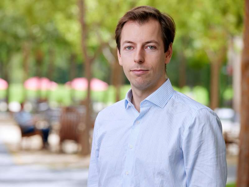 Fabian Nagel stands outdoors with blurred figures and trees in the background.