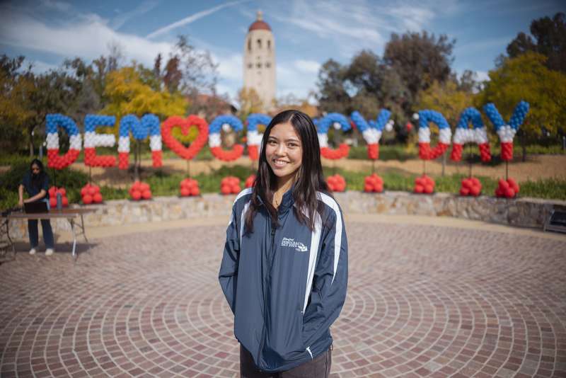 Student in front of Democracy Day balloon sign with Hoover Tower in the background