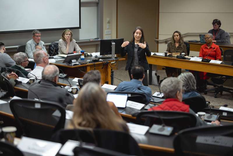 A member of the faculty engages the senate in a classroom setting, discussing topics while a panel looks on at the front of the room.