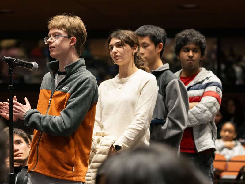 A group of students stands in line at a microphone during a Q&A session in an auditorium.