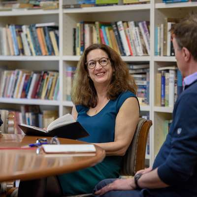 Three colleagues discuss a book around a library table.