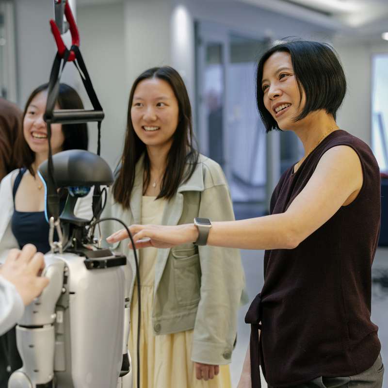 Karen Liu and a group of students gathered around a humanoid robot in a lab setting.