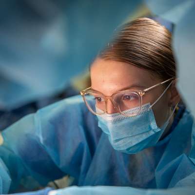 A medical student in blue surgical gear focuses on a task in a clinical setting.