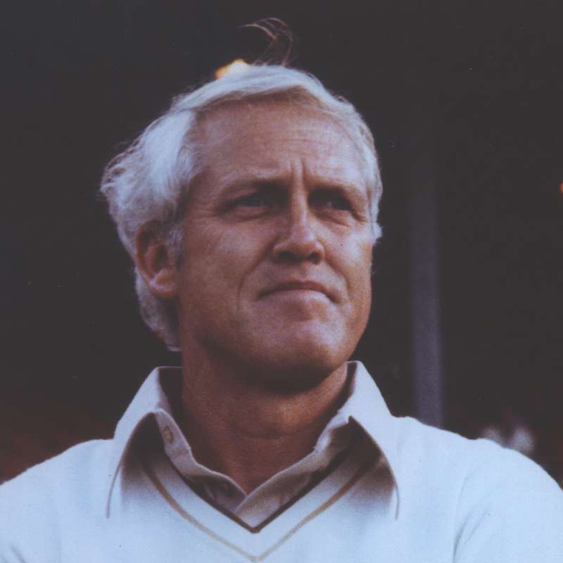 Stanford football head coach Bill Walsh standing outdoors in dim lighting, looking thoughtfully toward the distance.
