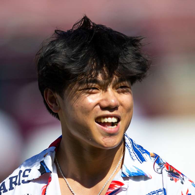 Asher Hong wearing a Paris Olympics shirt, smiling and looking away from the camera in an outdoor setting against a blurry background.