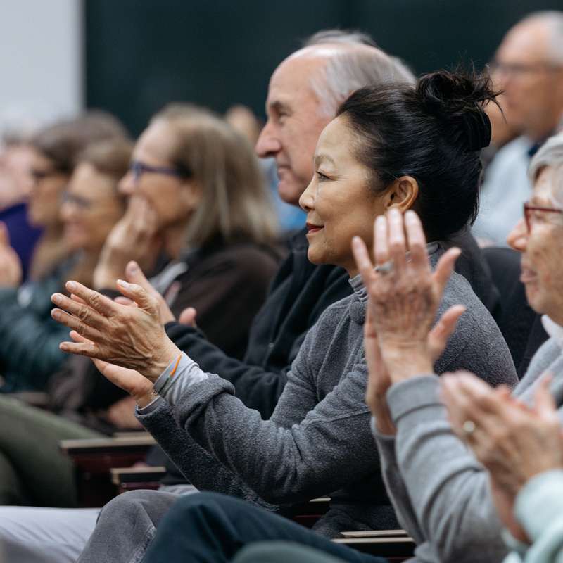 A diverse crowd of people clapping and showing appreciation during an event or presentation.
