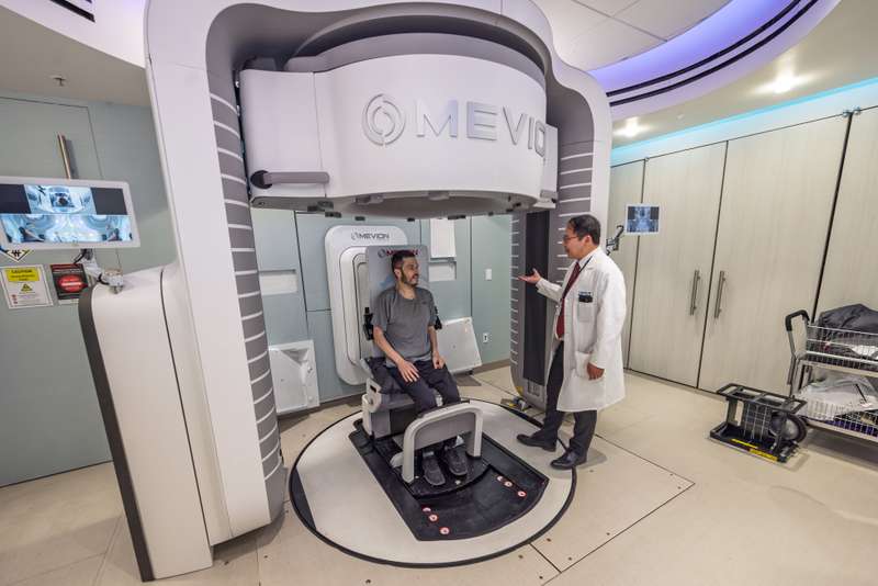 A doctor talks to a patient sitting who is sitting in a new piece of medical equipment