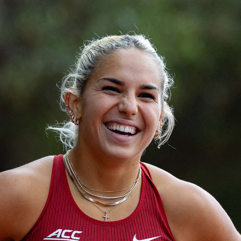 Sydney Barta in a Cardinal sports tank top and layered necklaces poses for a photo, smiling at the camera.