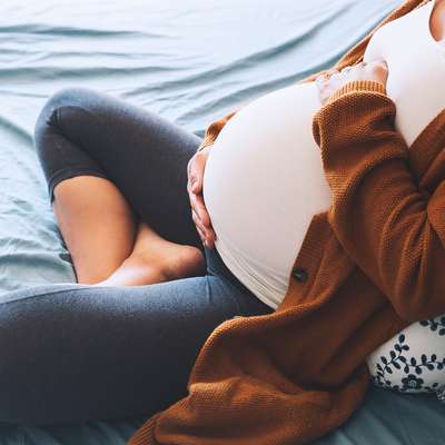 Pregnant woman on bed, holding her belly