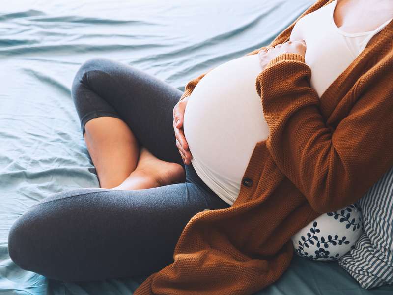 Pregnant woman on bed, holding her belly