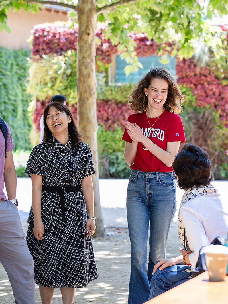 A group of students engaged in conversation outdoors, with a vibrant green and floral backdrop.
