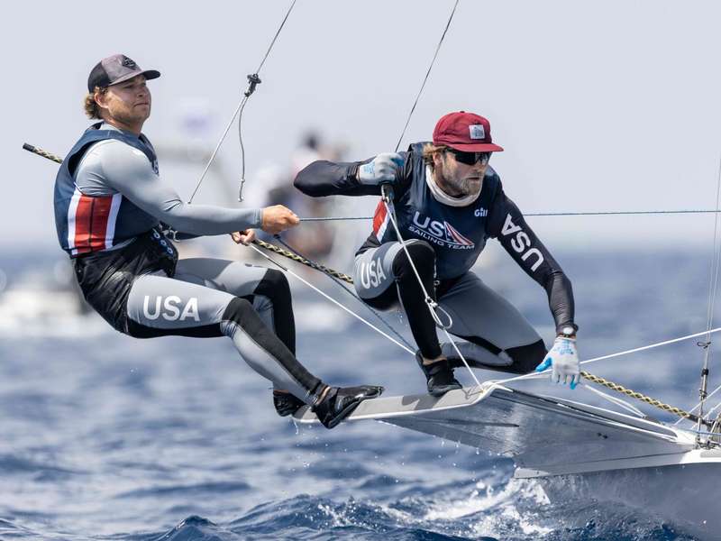 Two members of the U.S. men's sailing team pull on cables as they steer their boat across the water