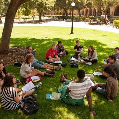 A group of students sits in a circle on the grass, discussing readings together outside near Stanford’s Main Quad.
