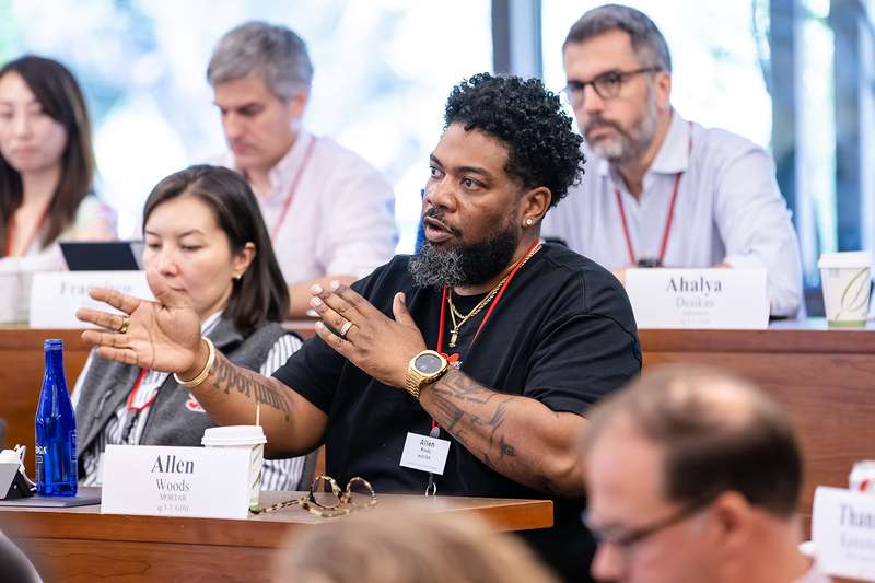 A participant actively engaging in discussion during a meeting, seated among others in a conference room with name tags visible.