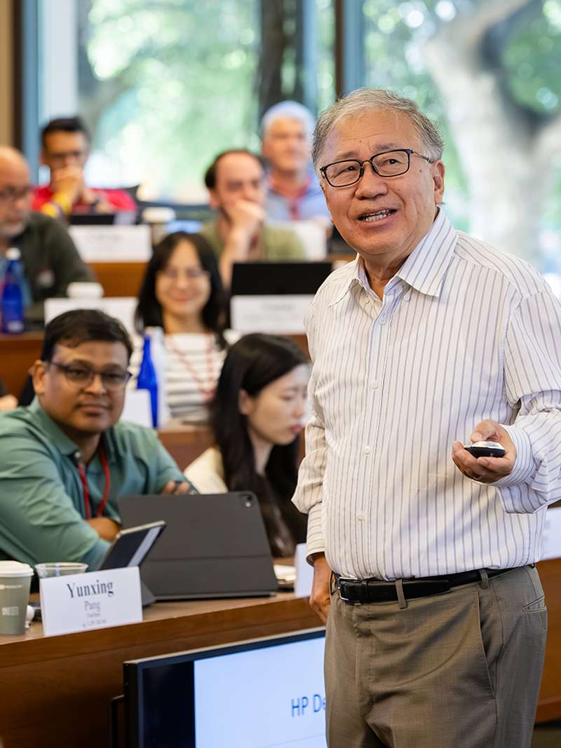 A presenter speaks to an audience in a classroom setting, with students engaged and taking notes during a lecture.
