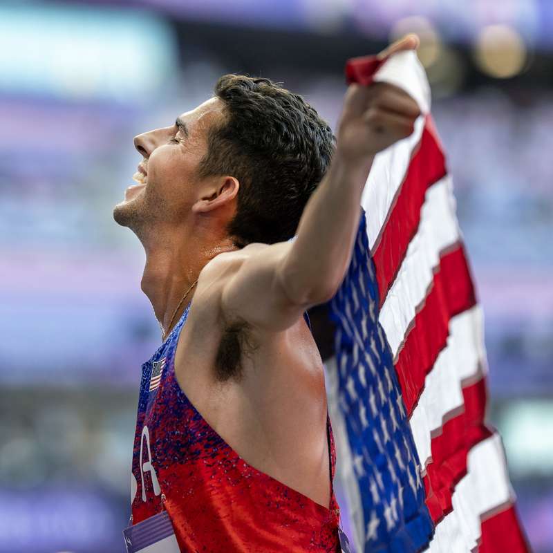 Grant Fisher closes his eyes and holds an American flag in celebration