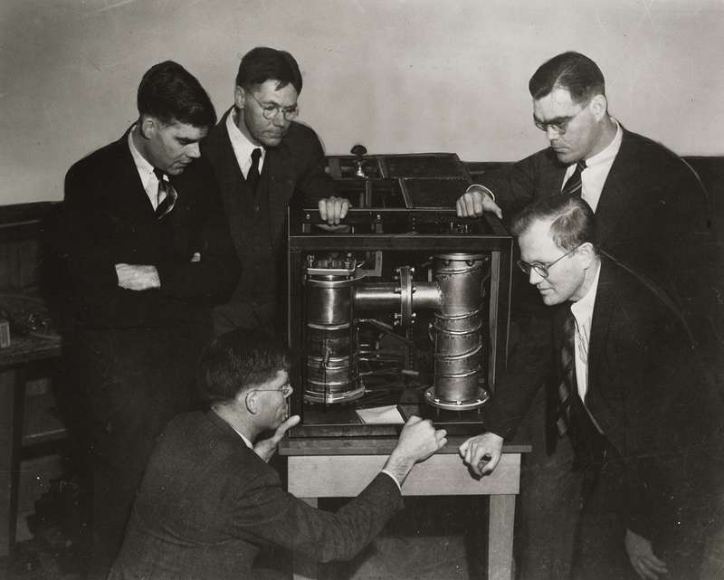 Stanford engineers examine an early klystron tube in a vintage black-and-white laboratory photograph.