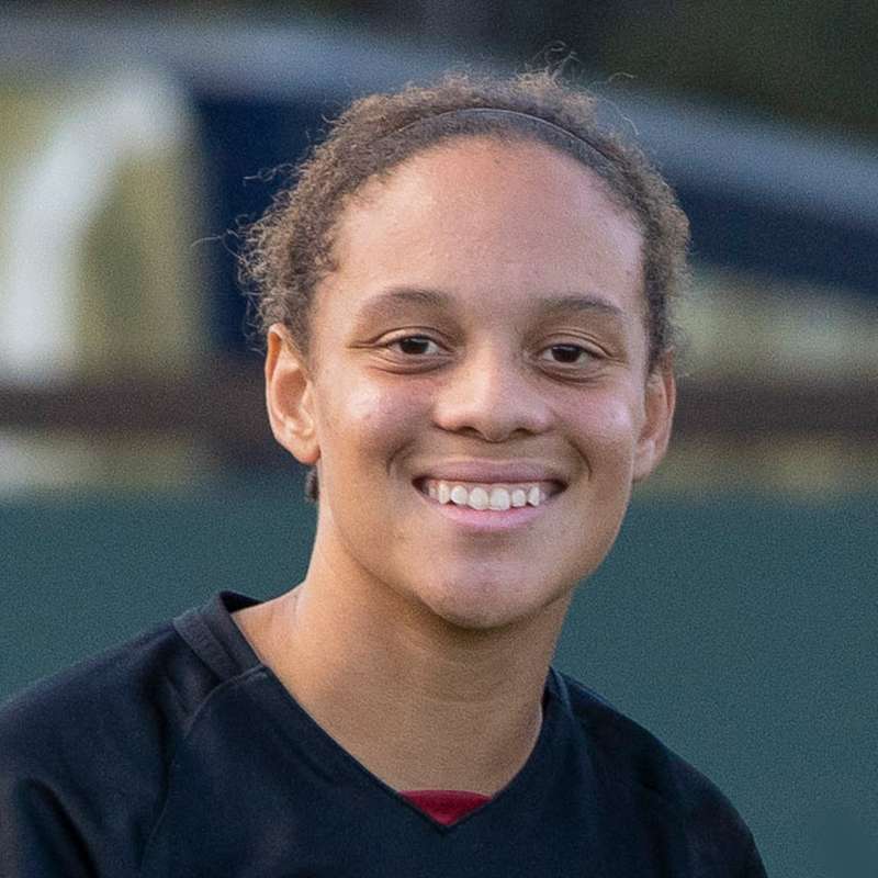 Jasmine Aikey standing in an outdoor setting against a blurry background, looking at the camera and smiling for the photo.