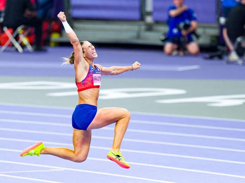 Valarie Allman leaps and pumps her fist in celebration on the track at the Paris 2024 Olympic Games, wearing a Team USA red top and blue shorts.