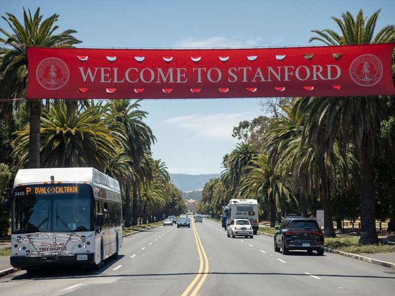 Welcome to Stanford banner over Palm Drive with a shuttle driving under it.
