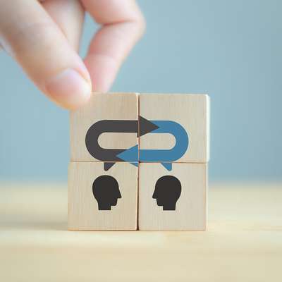 Wooden blocks show two head silhouettes connected by exchange arrows, symbolizing dialogue or communication between people.