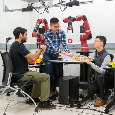 Three students work together in a lab setting to operate robotic arms.