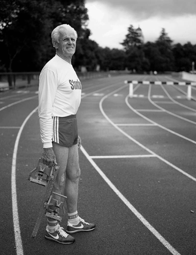 Black and white photo of longtime Stanford track and field coach Payton Jordan, who led the 1968 U.S. Olympic team standing on the track holding a starting block.