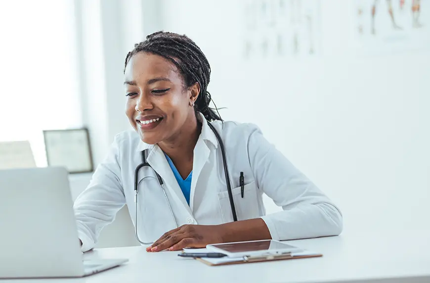 Smiling physician working on a laptop computer.