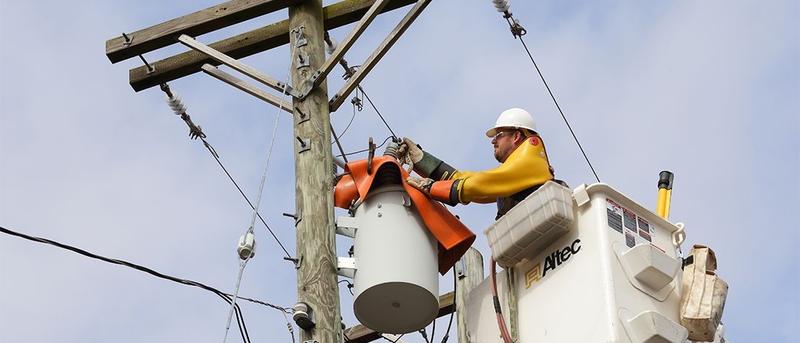 Utility worker in a bucket fixing the power line going to a transformer on a utility pole.