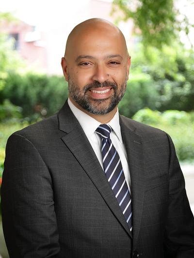 Abdul Aghil in a dark suit and striped tie, smiling.