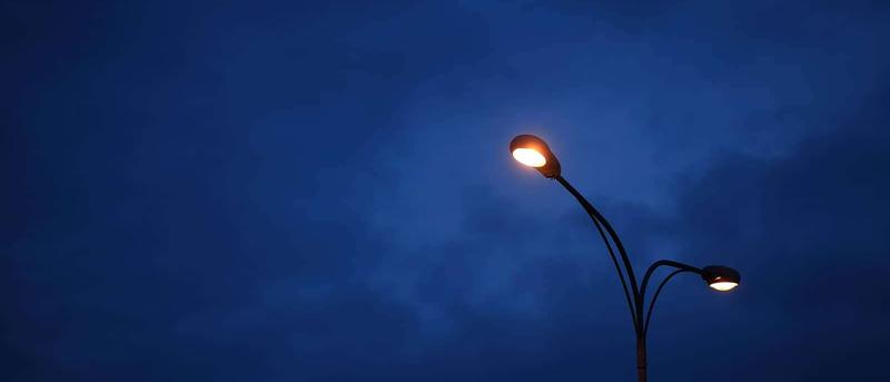 Two streetlights illuminate against a deep blue, cloudy evening sky.