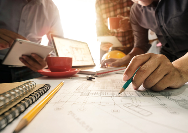 Three contractors sketching marketing ideas at a desk with coffee and laptops
