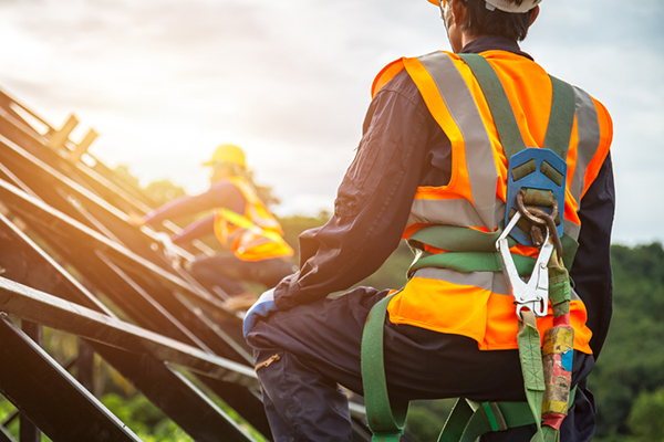 Two construction workers using safety harnesses while working on a roof frame