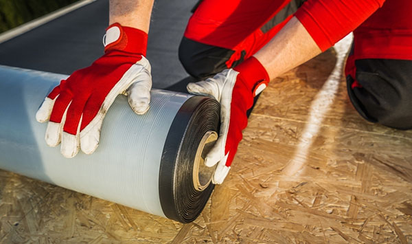 A roofing contractor prepares a roll of EPDM roof membrane material.